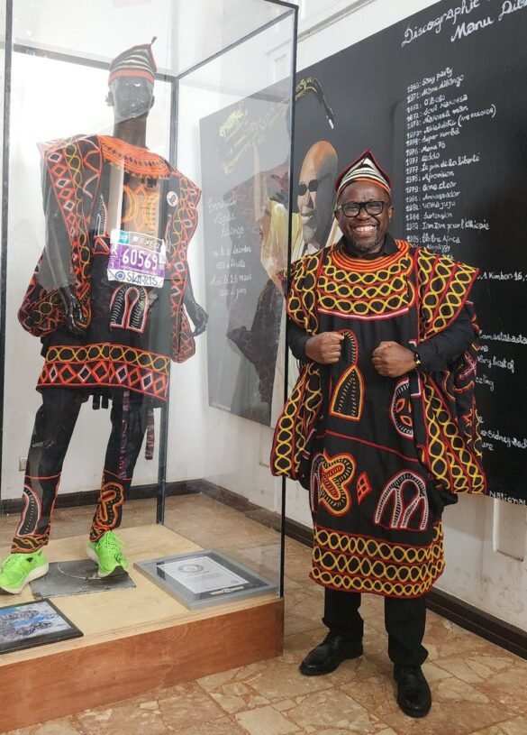Toghu Marathoner standing next to the donated Guinness World Records-winning Attire, CertifiToghu Marathoner standing next to the donated Guinness World Records-winning Attire, Certificate at the National Museum cate at the National Museum